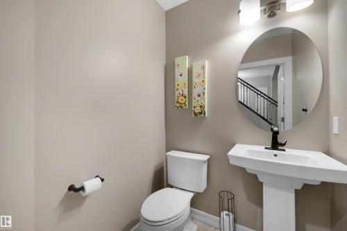 Pedestal sink with black faucet, round mirror, and two-light vanity fixture - 1507 Wates Place Sw, Edmonton, AB 