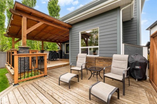 Expansive multi-level wood deck featuring a covered patio with a natural wood ceiling, wood railings with black metal spindles, and a charcoal gray siding exterior - 1507 Wates Place Sw, Edmonton, AB 
