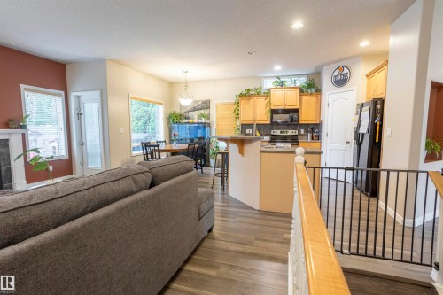 Open-concept living area with wood-finish flooring, a fireplace featuring a dark tile surround and white mantel, and a dining area with pendant lighting - 1441 Highwood Boulevard, Devon, AB 