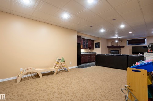 Versatile recreation room featuring patterned carpet flooring, recessed lighting, and a stone-faced fireplace with a mantel - 1441 Highwood Boulevard, Devon, AB 