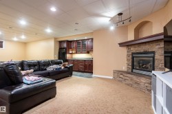 Living area featuring a stacked stone fireplace with a wood mantel, recessed lighting, drop ceiling, and a wet bar with dark wood cabinetry and a countertop - 
