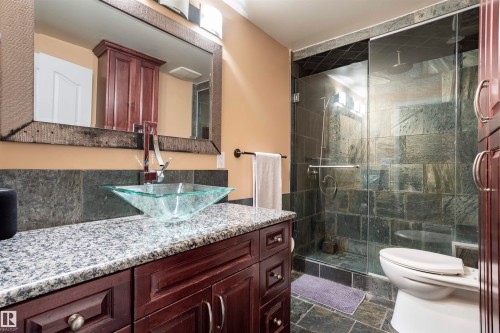 Bathroom featuring a glass vessel sink, granite countertop, rich wood-finish vanity, framed mirror, and a glass-enclosed shower with stone-look tile - 1441 Highwood Boulevard, Devon, AB 