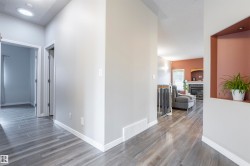 Wood-finish flooring extending through the hallway and into the living area, featuring recessed lighting, a built-in wall niche with integrated lighting, and white baseboards - 