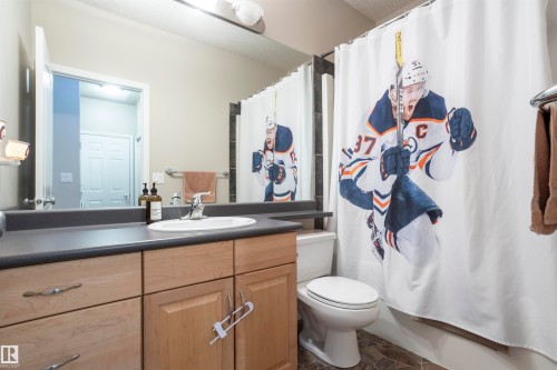 Bathroom featuring a single vanity with a white oval sink and chrome faucet, light wood-finish cabinetry, a dark countertop, and tiled flooring - 1441 Highwood Boulevard, Devon, AB 