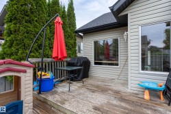 Spacious wooden deck featuring a slatted railing, mature evergreen trees providing privacy, and horizontal vinyl siding on the exterior - 
