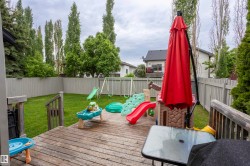 Expansive backyard featuring a wood deck, manicured lawn, and perimeter fencing - 