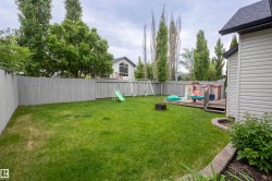 Expansive fenced backyard featuring a grassy lawn, a raised wood deck, and a stone-lined planter bed - 