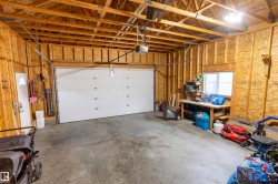 Spacious garage featuring an overhead door, exposed wood framing, concrete flooring, and a side entry door - 