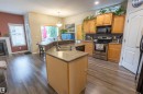 Kitchen featuring wood-finish flooring, a double basin sink, stainless steel appliances, wood cabinetry, and a grey tile backsplash - 1441 Highwood Boulevard, Devon, AB 