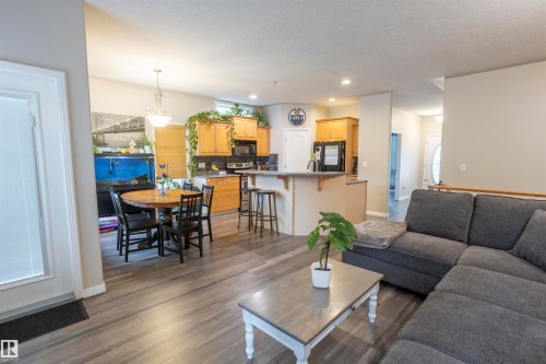 Open-concept living space with wood-finish flooring, a kitchen featuring light wood cabinetry and a breakfast bar, and a dining area with an overhead chandelier - 1441 Highwood Boulevard, Devon, AB 