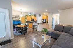 Open-concept living space with wood-finish flooring, a kitchen featuring light wood cabinetry and a breakfast bar, and a dining area with an overhead chandelier - 
