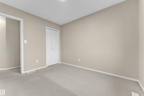 Neutral-toned interior room featuring light beige walls and carpeting, white baseboards, and a white bi-fold closet door - 3134 30 Avenue Nw, Edmonton, AB 