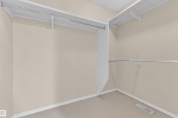 Spacious walk-in closet featuring built-in shelving, multiple hanging rods, neutral wall color, and light-toned carpeting - 