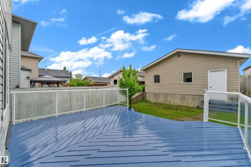 Expansive blue-stained wood deck with white posts and glass panel railing - 3134 30 Avenue Nw, Edmonton, AB 