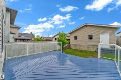 Expansive blue-stained wood deck with white posts and glass panel railing - 