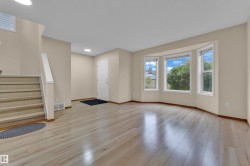 Bright living area featuring light wood-finish flooring, a bay window with multiple panes, neutral wall tones, and a staircase with white risers and handrail - 