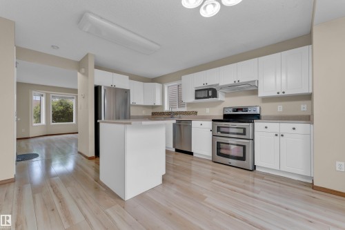 Bright kitchen featuring white cabinetry, stainless steel appliances, wood-finish flooring, a central island, and a mosaic tile backsplash - 3134 30 Avenue Nw, Edmonton, AB 