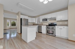 Bright kitchen featuring white cabinetry, stainless steel appliances, wood-finish flooring, a central island, and a mosaic tile backsplash - 