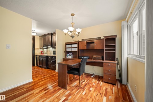 Warm-toned wood-finish flooring extending into the kitchen, featuring a built-in wooden desk unit with integrated shelving - 31 Royal Road, Edmonton, AB 