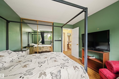 Bedroom featuring wood-finish flooring, a white paneled door, and a mirrored closet with a light wood frame - 31 Royal Road, Edmonton, AB 
