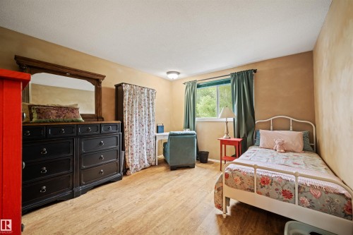 Interior room with wood-finish flooring, a window with green drapes, a built-in closet with patterned curtains, and neutral-toned walls - 31 Royal Road, Edmonton, AB 
