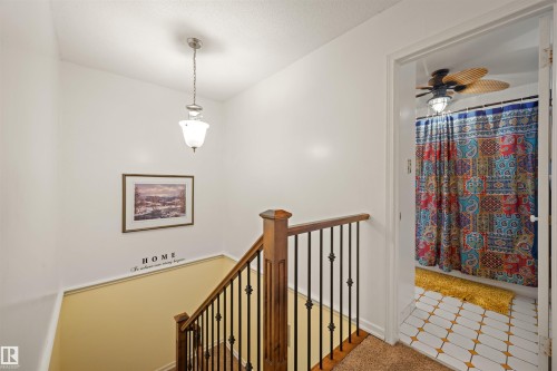 Staircase featuring wood handrails and wrought iron balusters, with a ceiling pendant light fixture - 31 Royal Road, Edmonton, AB 