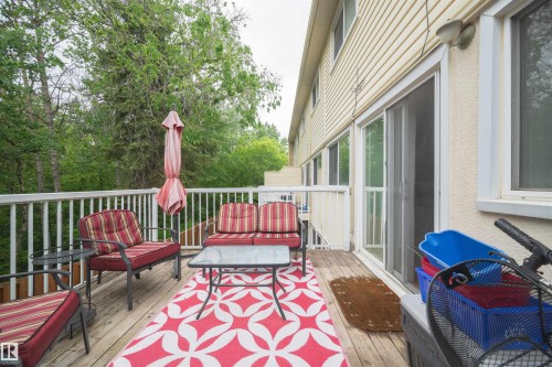 Expansive wood deck with white railings, featuring a sliding glass patio door, exterior wall sconce, and textured exterior siding - 31 Royal Road, Edmonton, AB 