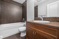 Bathroom featuring a wood-finish vanity with an integrated sink, a mosaic tile backsplash, and a large wall-mounted mirror - 