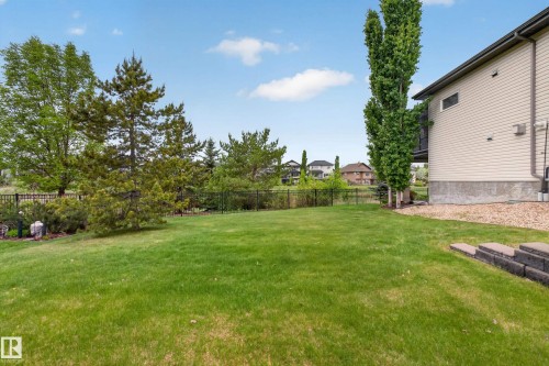 Expansive rear yard featuring green lawn, mature trees, a black metal fence, and a gravel perimeter alongside the property - 624 Cantor Landing Landing, Edmonton, AB 