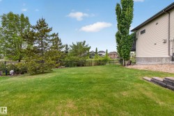 Expansive rear yard featuring green lawn, mature trees, a black metal fence, and a gravel perimeter alongside the property - 