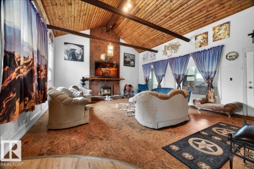 Spacious living area featuring a vaulted wood-plank ceiling with exposed beams, a brick-surround fireplace, and a wood mantel - 140 50047 Rge Rd 244, Rural Leduc County, AB 