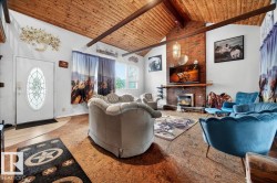 Spacious living area featuring a vaulted wood-plank ceiling with exposed beams, a prominent brick fireplace with a wood mantel, and large windows providing natural light - 