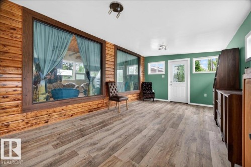Spacious interior featuring wood-finish flooring, accent wall with horizontal wood paneling, large picture windows, and a white entry door with clear glass insert - 140 50047 Rge Rd 244, Rural Leduc County, AB 