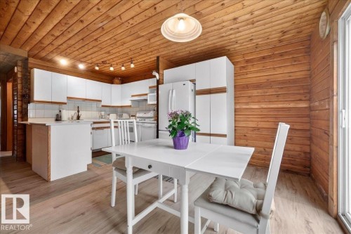 Open-concept kitchen and dining area featuring natural wood paneling on walls and ceiling, light wood-finish flooring, white cabinetry, track lighting, and a sliding glass door - 140 50047 Rge Rd 244, Rural Leduc County, AB 