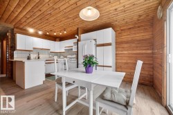 Open-concept kitchen and dining area featuring natural wood paneling on walls and ceiling, light wood-finish flooring, white cabinetry, track lighting, and a sliding glass door - 