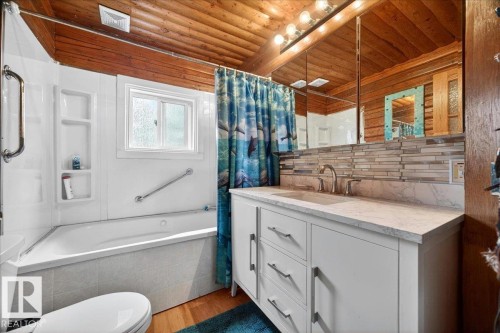 Bathroom featuring a wood-panel ceiling, white vanity with a light-toned countertop, modern chrome faucet, and a horizontally stacked tile backsplash - 140 50047 Rge Rd 244, Rural Leduc County, AB 