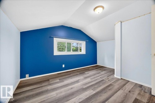 Room featuring wood-finish flooring, a vaulted ceiling, a single window, and a flush mount light fixture - 140 50047 Rge Rd 244, Rural Leduc County, AB 