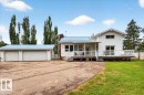White exterior with a light blue metal roof, featuring a multi-car garage, expansive driveway, and a large deck with white railings - 140 50047 Rge Rd 244, Rural Leduc County, AB 