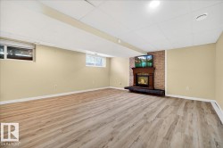 Finished lower level featuring wood-finish flooring, a brick fireplace surround with a wood mantel, and recessed lighting - 