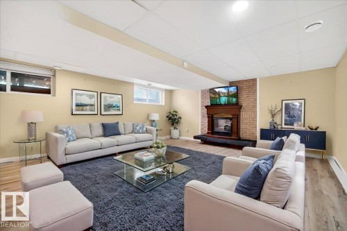 Finished basement area featuring wood-finish flooring, a brick-surround fireplace with a wood mantle, and a drop ceiling with recessed lighting - 140 50047 Rge Rd 244, Rural Leduc County, AB 
