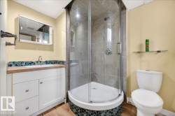 Full bathroom featuring a corner shower with glass enclosure, white vanity with integrated sink, teal mosaic tile backsplash, and wood-finish flooring - 