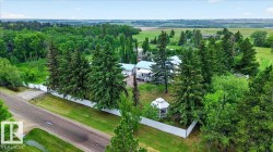 Expansive property featuring a white privacy fence, mature evergreen trees, a white outdoor gazebo, and distant cultivated fields - 