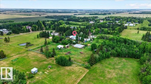 Aerial view of a rural landscape featuring expansive green fields, scattered residential structures, and mature tree lines - 140 50047 Rge Rd 244, Rural Leduc County, AB 