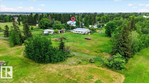 Expansive green spaces define this property, featuring a primary residence with a light-colored exterior and a prominent red roof - 140 50047 Rge Rd 244, Rural Leduc County, AB 