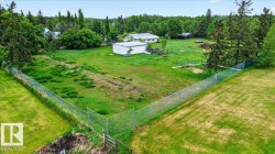 Expansive green space featuring chain-link fencing, mature trees, and outbuildings - 
