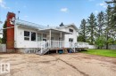 White siding exterior with a blue metal roof, featuring a red brick chimney, an elevated wood deck with white railings, and a covered porch area - 140 50047 Rge Rd 244, Rural Leduc County, AB 