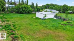 Expansive green space featuring a white outbuilding with a metal roof, surrounded by mature trees - 