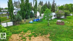 Expansive green space featuring mature trees, a chain-link fence, and a distant structure - 