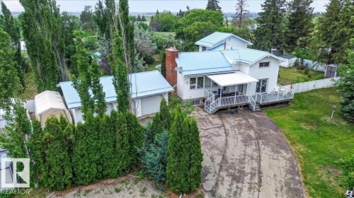 White exterior residence featuring a light blue metal roof, attached two-car garage, expansive deck, and a partially covered patio area - 140 50047 Rge Rd 244, Rural Leduc County, AB 
