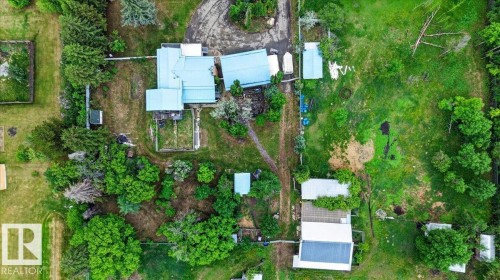 Expansive property featuring multiple structures, mature trees, open green spaces, a main residence with a light-colored roof, and a visible driveway - 140 50047 Rge Rd 244, Rural Leduc County, AB 